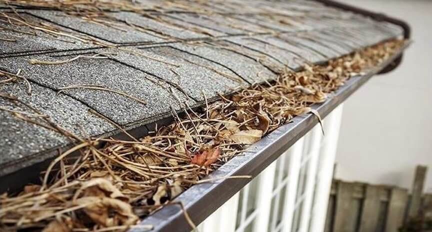 Clogged gutters overflowing and causing water damage to home foundation